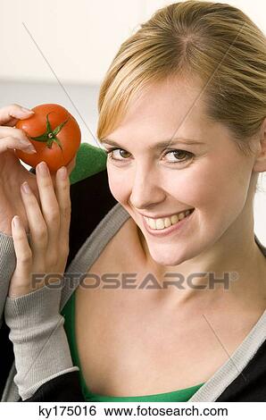 Stock Photograph - Portrait of a young woman showing a tomato. Fotosearch