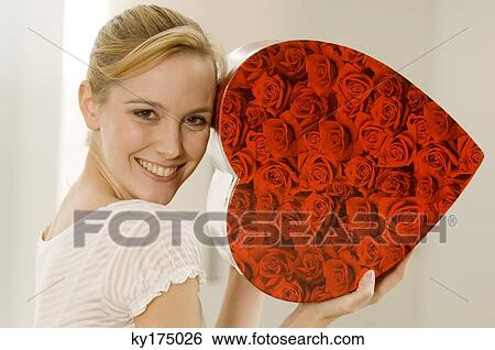 Portrait of a young woman showing a heart shape gift and smiling View Large Photo Image Stock Photograph - Portrait of a young woman showing a heart shape gift and smiling. Fotosearch