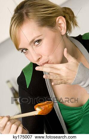 Stock Photo - Portrait of a young woman tasting tomato sauce with her finger. Fotosearch