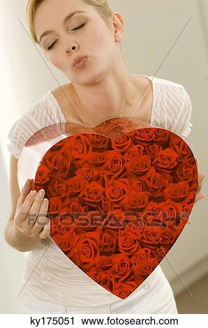 Young woman holding a heart shape gift and puckering her lips View Large Photo Image Stock Image - Young woman holding a heart shape gift and puckering her lips. Fotosearch