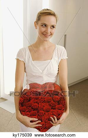 Young woman holding a heart shape gift and smiling View Large Photo Image Stock Photo - Young woman holding a heart shape gift and smiling. Fotosearch