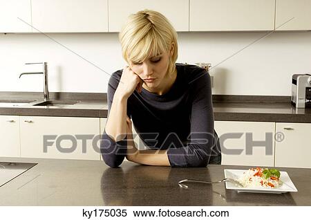 Stock Photography - Young woman leaning against a kitchen counter and thinking. Fotosearch