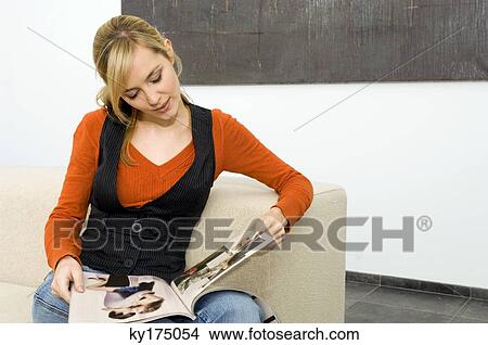 Young woman sitting on a couch and reading a magazine View Large Photo Image Picture - Young woman sitting on a couch and reading a magazine. Fotosearch