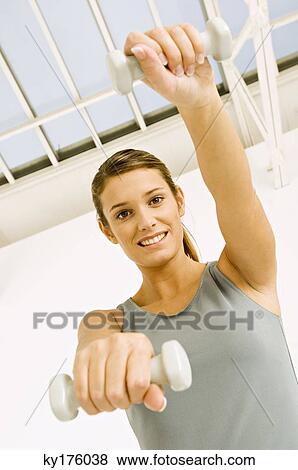 Portrait of a young woman exercising with dumbbells View Large Photo Image Stock Photo - Portrait of a young woman exercising with dumbbells. Fotosearch