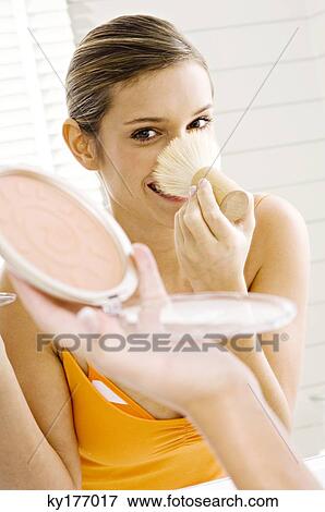 Stock Photo - Reflection of a young woman applying make-up on her face. Fotosearch