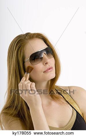 Close-up of a young woman applying make-up on her cheek View Large Photo Image Stock Photography - Close-up of a young woman applying make-up on her cheek. Fotosearch