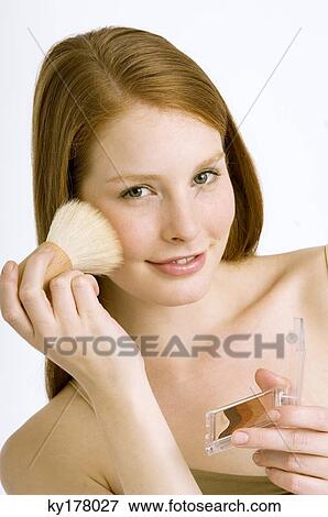 Portrait of a young woman applying blush on her cheek View Large Photo Image Stock Photo - Portrait of a young woman applying blush on her cheek. Fotosearch