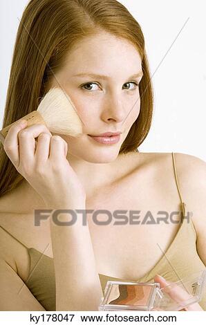 Portrait of a young woman applying blush on her cheek View Large Photo Image Stock Photo - Portrait of a young woman applying blush on her cheek. Fotosearch