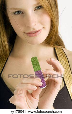 Stock Image - Portrait of a young woman filing her nails and smiling. Fotosearch