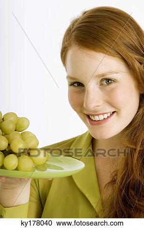 Portrait of a young woman holding a plate of grapes and smiling View Large Photo Image Stock Image - Portrait of a young woman holding a plate of grapes and smiling. Fotosearch