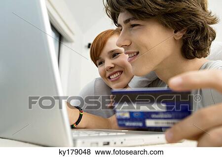 Close-up of a teenage boy holding a credit card and using a laptop with a young woman sitting beside him View Large Photo Image Stock Photo - Close-up of a teenage boy holding a credit card and using a laptop with a young woman sitting beside him. Fotosearch