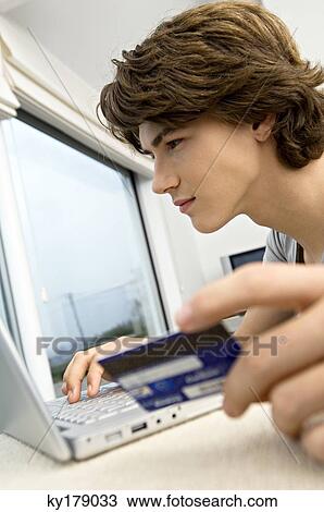 Close-up of a teenage boy using a laptop and holding a credit card View Large Photo Image Stock Image - Close-up of a teenage boy using a laptop and holding a credit card. Fotosearch