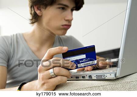 Close-up of a teenage boy using a laptop and holding a credit card View Large Photo Image Stock Photography - Close-up of a teenage boy using a laptop and holding a credit card. Fotosearch
