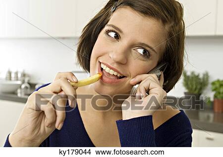 Close-up of a young woman eating French fries and talking on a mobile phone View Large Photo Image Picture - Close-up of a young woman eating French fries and talking on a mobile phone. Fotosearch