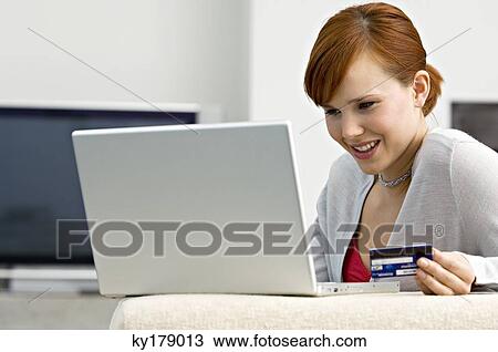 Stock Image - Close-up of a young woman holding a credit card and using a laptop. Fotosearch