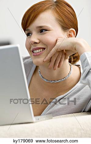 Close-up of a young woman sitting in front of a laptop and smiling View Large Photo Image Stock Photo - Close-up of a young woman sitting in front of a laptop and smiling. Fotosearch