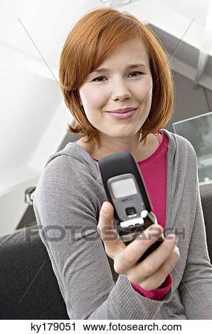 Close-up of a young woman sitting on a couch and using a mobile phone View Large Photo Image Stock Image - Close-up of a young woman sitting on a couch and using a mobile phone. Fotosearch
