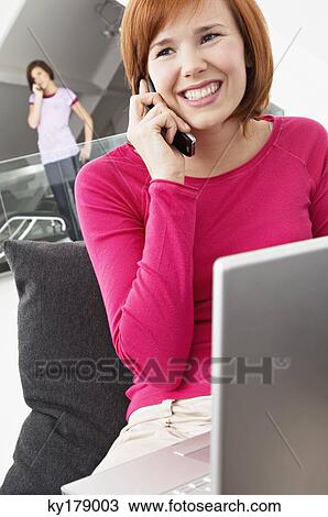Close-up of a young woman using a laptop and talking on a mobile phone View Large Photo Image Stock Image - Close-up of a young woman using a laptop and talking on a mobile phone. Fotosearch