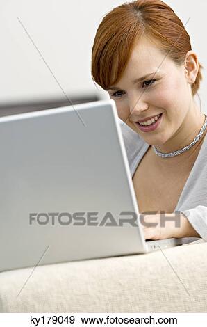 Close-up of a young woman using a laptop and smiling View Large Photo Image Stock Photo - Close-up of a young woman using a laptop and smiling. Fotosearch