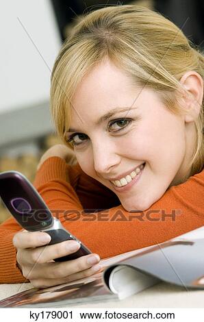 Stock Image - Portrait of a young woman holding a mobile phone and smiling. Fotosearch