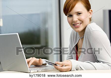 Portrait of a young woman holding a credit card and using a laptop View Large Photo Image Stock Photo - Portrait of a young woman holding a credit card and using a laptop. Fotosearch