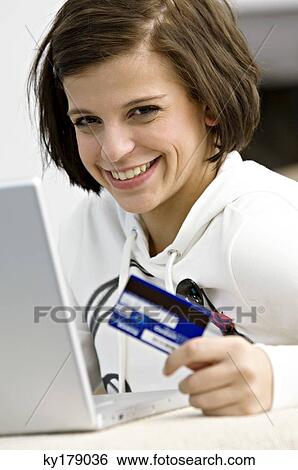 Stock Photograph - Portrait of a young woman holding a credit card and using a laptop. Fotosearch