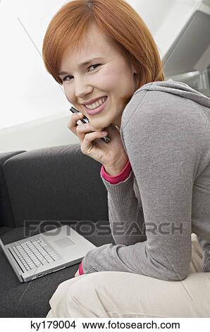 Picture - Portrait of a young woman using a mobile phone and smiling. Fotosearch