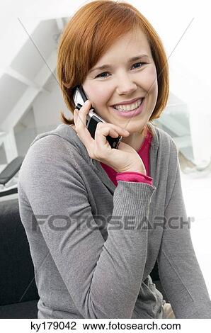 Stock Image - Portrait of a young woman using a mobile phone and smiling. Fotosearch