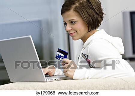 Side profile of a young woman holding a credit card and using a laptop View Large Photo Image Stock Photo - Side profile of a young woman holding a credit card and using a laptop. Fotosearch
