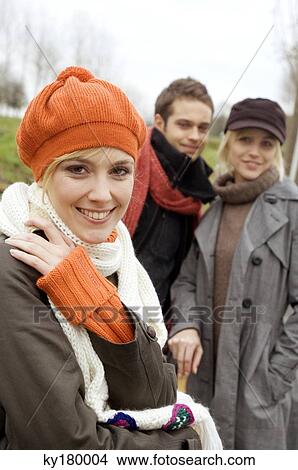 Picture - Close-up of a young woman smiling with her friends standing in the background. Fotosearch