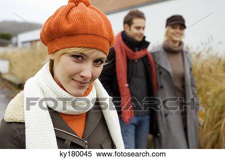 Stock Photography - Close-up of a young woman smiling with her friends standing in the background. Fotosearch