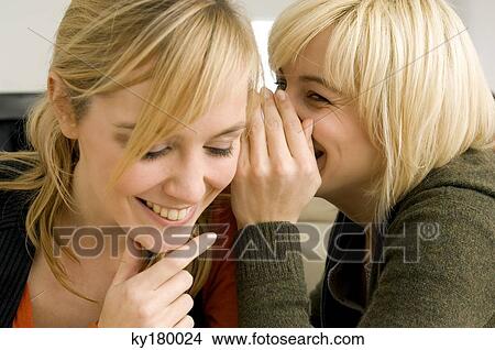 Close-up of a young woman whispering to her friend View Large Photo Image Picture - Close-up of a young woman whispering to her friend. Fotosearch