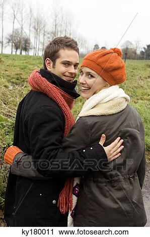Portrait of a young couple standing with arm around each other and smiling View Large Photo Image Stock Image - Portrait of a young couple standing with arm around each other and smiling. Fotosearch