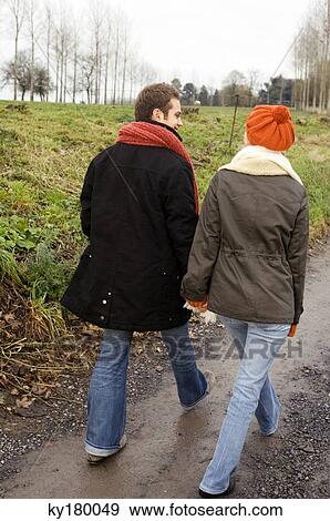 Stock Photo - Rear view of a young couple walking on a dirt road. Fotosearch