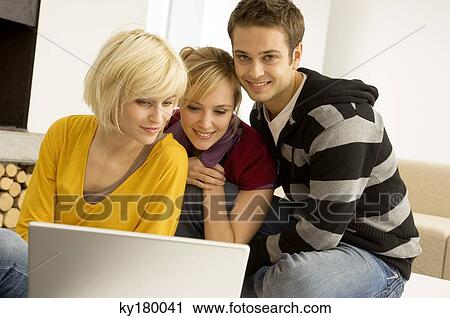 Stock Image - Two young women and a young man sitting in front of a laptop and smiling. Fotosearch