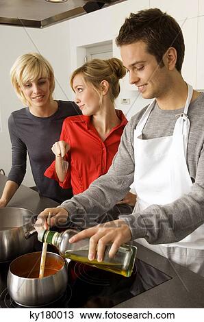 Two young women and a young man preparing food in the kitchen View Large Photo Image Stock Image - Two young women and a young man preparing food in the kitchen. Fotosearch
