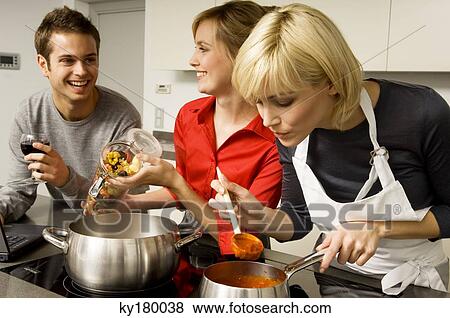 Two young women and a young man preparing food in the kitchen View Large Photo Image Stock Photo - Two young women and a young man preparing food in the kitchen. Fotosearch