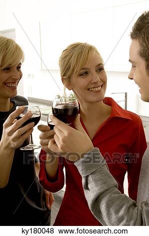 Stock Photo - Two young women and a young man toasting with wine glasses. Fotosearch