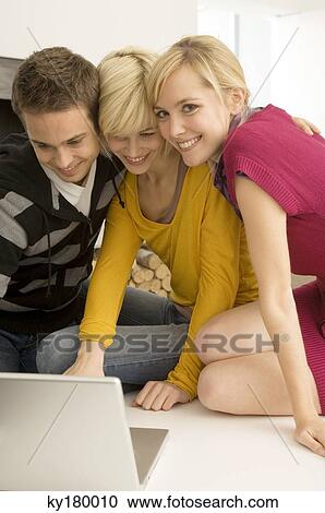 Two young women and a young man using a laptop and smiling View Large Photo Image Stock Image - Two young women and a young man using a laptop and smiling. Fotosearch