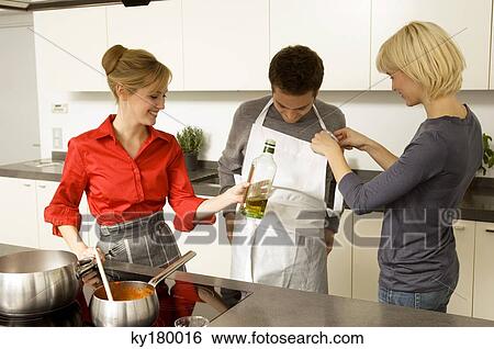 Two young women helping a young man in wearing an apron in the kitchen View Large Photo Image Stock Photograph - Two young women helping a young man in wearing an apron in the kitchen. Fotosearch