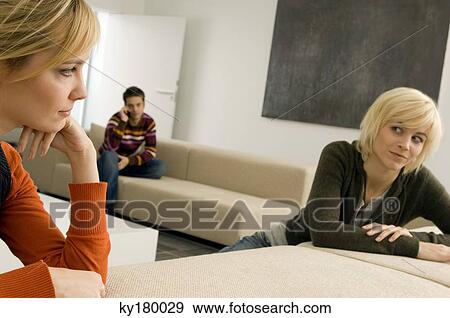Two young women looking at each other with a young man sitting in the background View Large Photo Image Stock Photo - Two young women looking at each other with a young man sitting in the background. Fotosearch