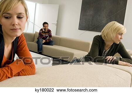 Two young women thinking with a young man sitting in the background View Large Photo Image Stock Image - Two young women thinking with a young man sitting in the background. Fotosearch