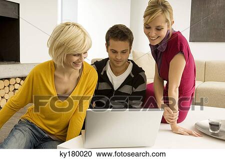 Young man with two young women looking at a laptop View Large Photo Image Stock Image - Young man with two young women looking at a laptop. Fotosearch