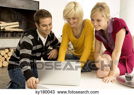 Stock Image - Young man with two young women looking at a laptop and smiling. Fotosearch