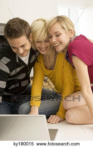 Young man with two young women looking at a laptop and smiling View Large Photo Image Stock Photography - Young man with two young women looking at a laptop and smiling. Fotosearch