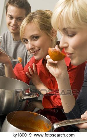 Young woman tasting tomato sauce with a ladle with a young man and a young woman beside her in the kitchen View Large Photo Image Stock Photo - Young woman tasting tomato sauce with a ladle with a young man and a young woman beside her in the kitchen. Fotosearch