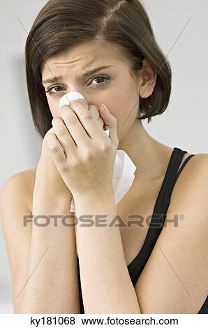 Stock Photo - Portrait of a young woman blowing her nose. Fotosearch