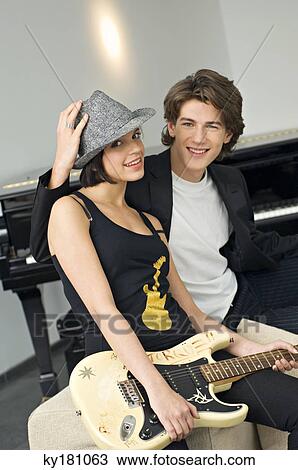 Portrait of a young woman holding a guitar with a teenage boy sitting beside her View Large Photo Image Stock Image - Portrait of a young woman holding a guitar with a teenage boy sitting beside her. Fotosearch