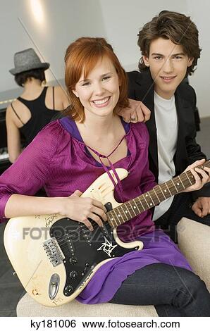 Portrait of a young woman playing a guitar with a teenage boy sitting beside her View Large Photo Image Stock Photograph - Portrait of a young woman playing a guitar with a teenage boy sitting beside her. Fotosearch