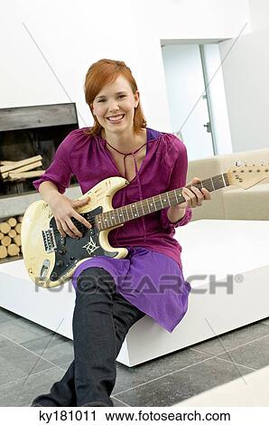 Portrait of a young woman sitting with a guitar on a coffee table and smiling View Large Photo Image Stock Image - Portrait of a young woman sitting with a guitar on a coffee table and smiling. Fotosearch